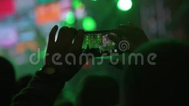 手在人群中拿着智能手机和拍摄音乐表演.. 舞台上明亮的灯光